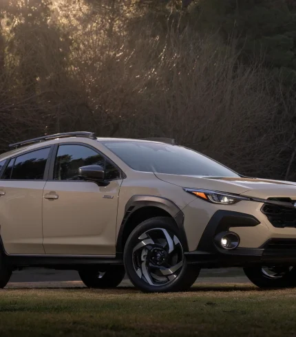 Передній ракурс 3/4 Subaru Crosstrek Hybrid 2026 року пісочного кольору на фоні вечірнього лісу.